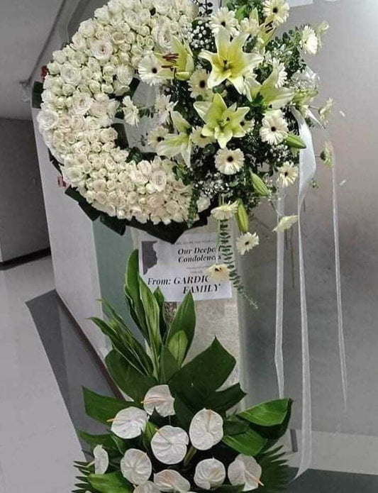 Circular arrangement for Purity Condolences. Featuring Radus, Yellow Win, Gerbera, Gypsophila, and Anthurium flowers, this elegant arrangement accented with Eucalyptus, Abaca Leaves, Fortune Plant Leaves, Anahaw Leaves, Greenline Leaves, and Tibatib Leaves expresses sympathy and honors the purity of the departed.