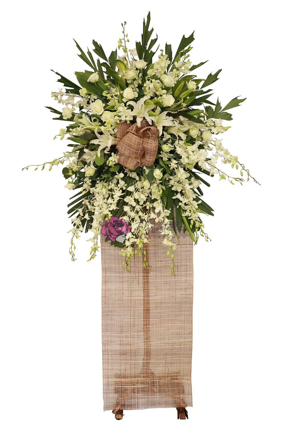 Funeral flower stand with white flowers symbolizing peace and respect. The arrangement includes orchids, casa blanca lilies, and white roses, accented with fishtail and ducktail leaves. This peaceful display conveys condolences and is suitable for a funeral service.